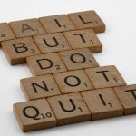 Close-up of Scrabble tiles forming the motivational phrase 'Fail but do not quit' on a white surface.